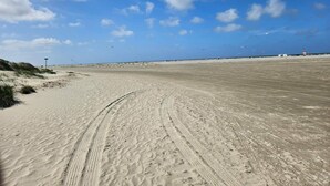 A wide sandy beach with tire tracks, a clear blue sky, and a distant lighthouse. - 4 Person Holiday Home in Fano (Fano)