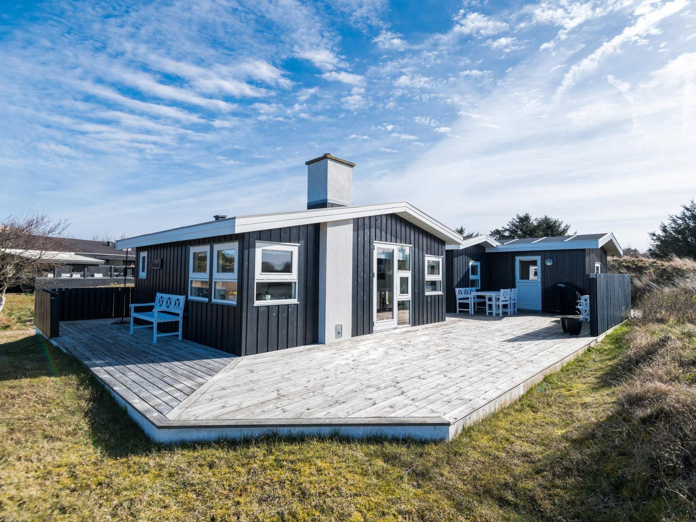 Ein modernes Haus mit einer Terrasse, einem überdachten Sitzbereich im Freien und einem umzäunten Garten.