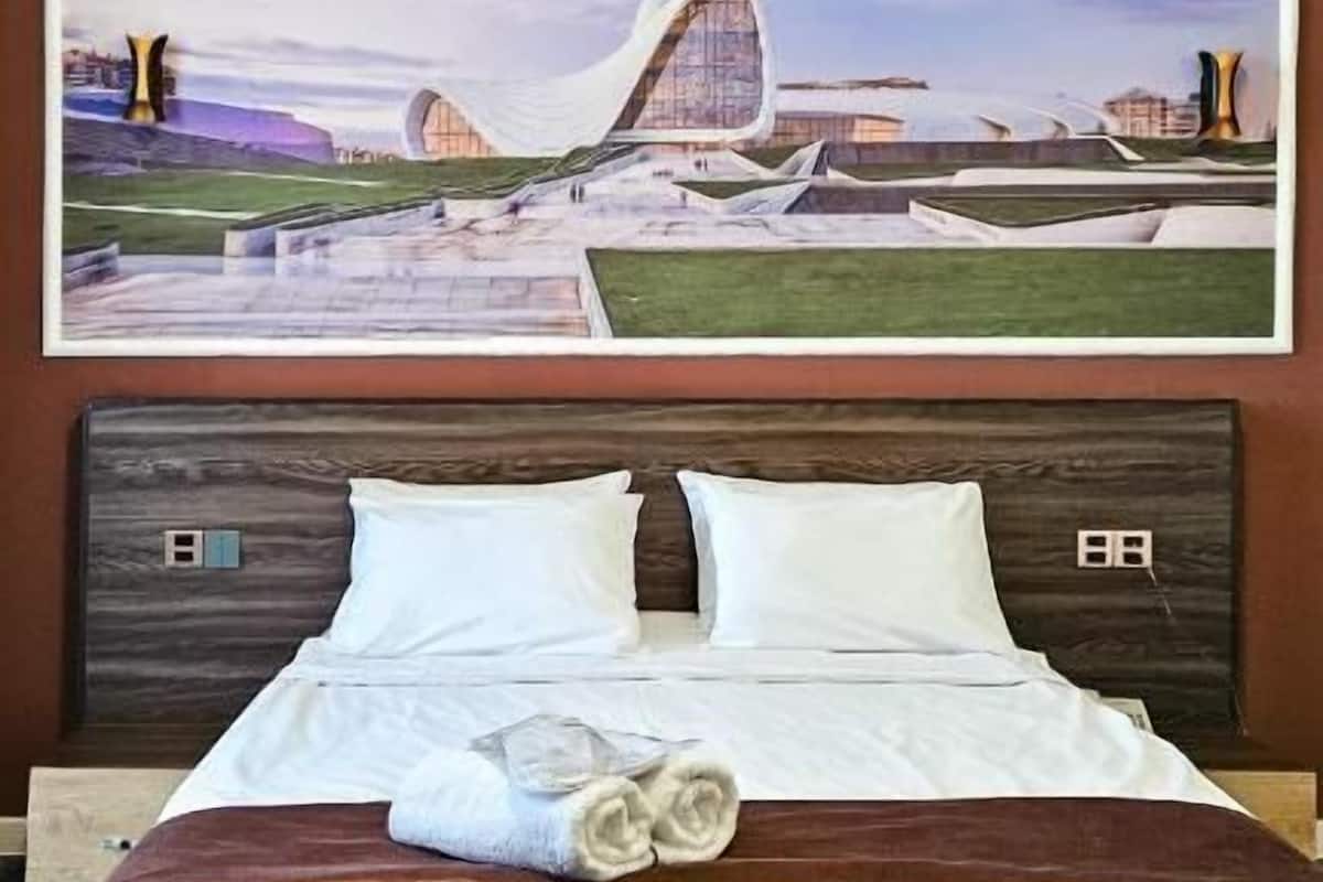 A hotel room with a bed, pillows, and a large painting of a building on the wall.
