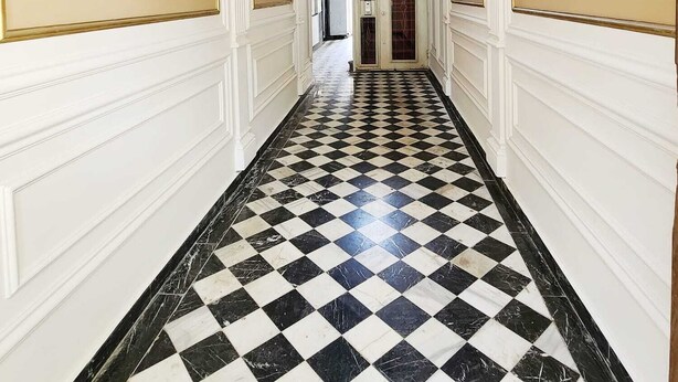 En hall med ett rutmönstrat golv, vita väggar och guldfärgade detaljer.