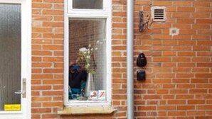 Un bâtiment en briques avec une fenêtre, une porte et une petite grille d’aération sur le mur.