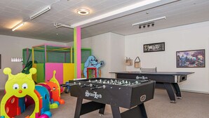 Une pièce équipée de deux tables de baby-foot, de structures de jeux colorées et d’une table de ping-pong.