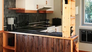 Een keuken met een houten kookeiland, een fornuis, hangend keukengerei en een krijtbordmenu.