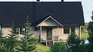 Een houten chalet met een puntige dak en een veranda, en een kleine trap naar de ingang.