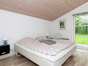 A bedroom with a bed, a nightstand, a lamp, a window with a view of greenery, and a painting on the wall. - 6 Person Holiday Home in Veslos (Vesløs)