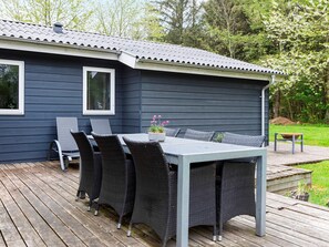 A deck with a table and chairs, a small garden area, and a building with a dark exterior. - 6 Person Holiday Home in Veslos (Vesløs)