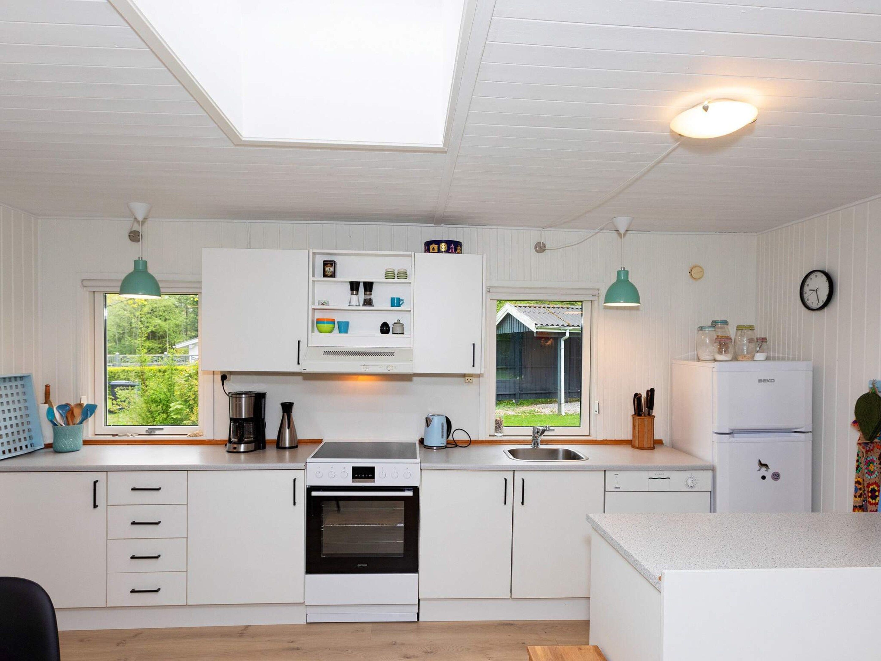 Una cocina moderna con armarios blancos, horno empotrado, pileta y ventana con vista a un jardín.