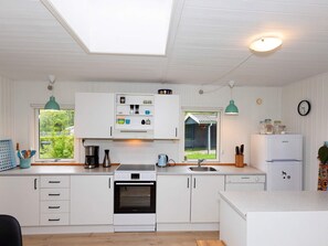 Une cuisine moderne avec des meubles blancs, un four encastré, un évier et une fenêtre donnant sur un jardin.