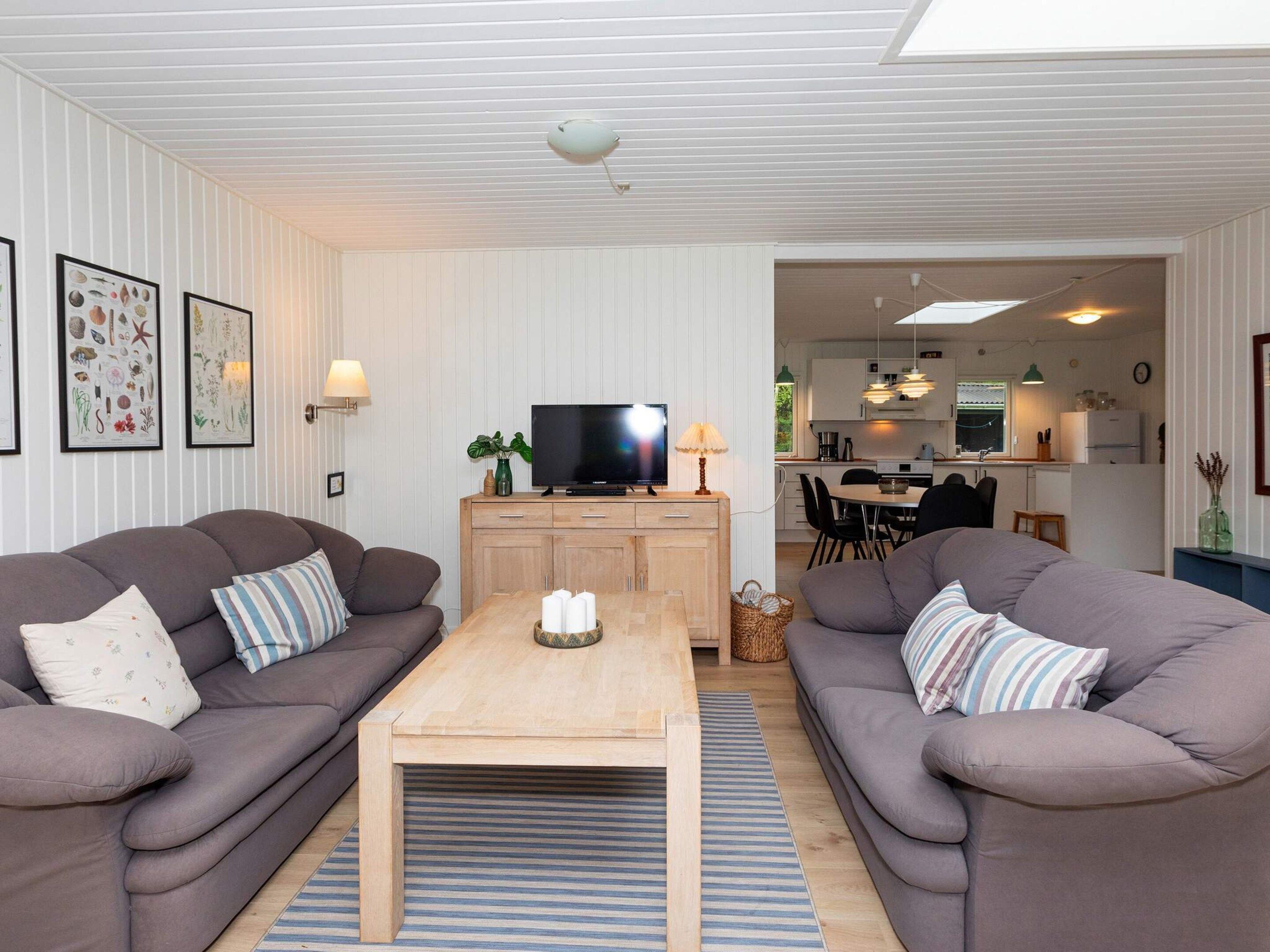 A modern living room with two sofas, a coffee table, and a TV. There is a kitchen visible in the background.