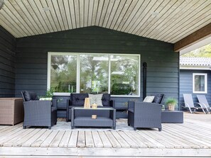 Un espace extérieur abrité, aménagé avec du mobilier aux couleurs sombres et doté d’une grande fenêtre.
