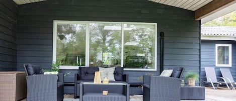 A covered outdoor seating area with dark-colored furniture and a large window.