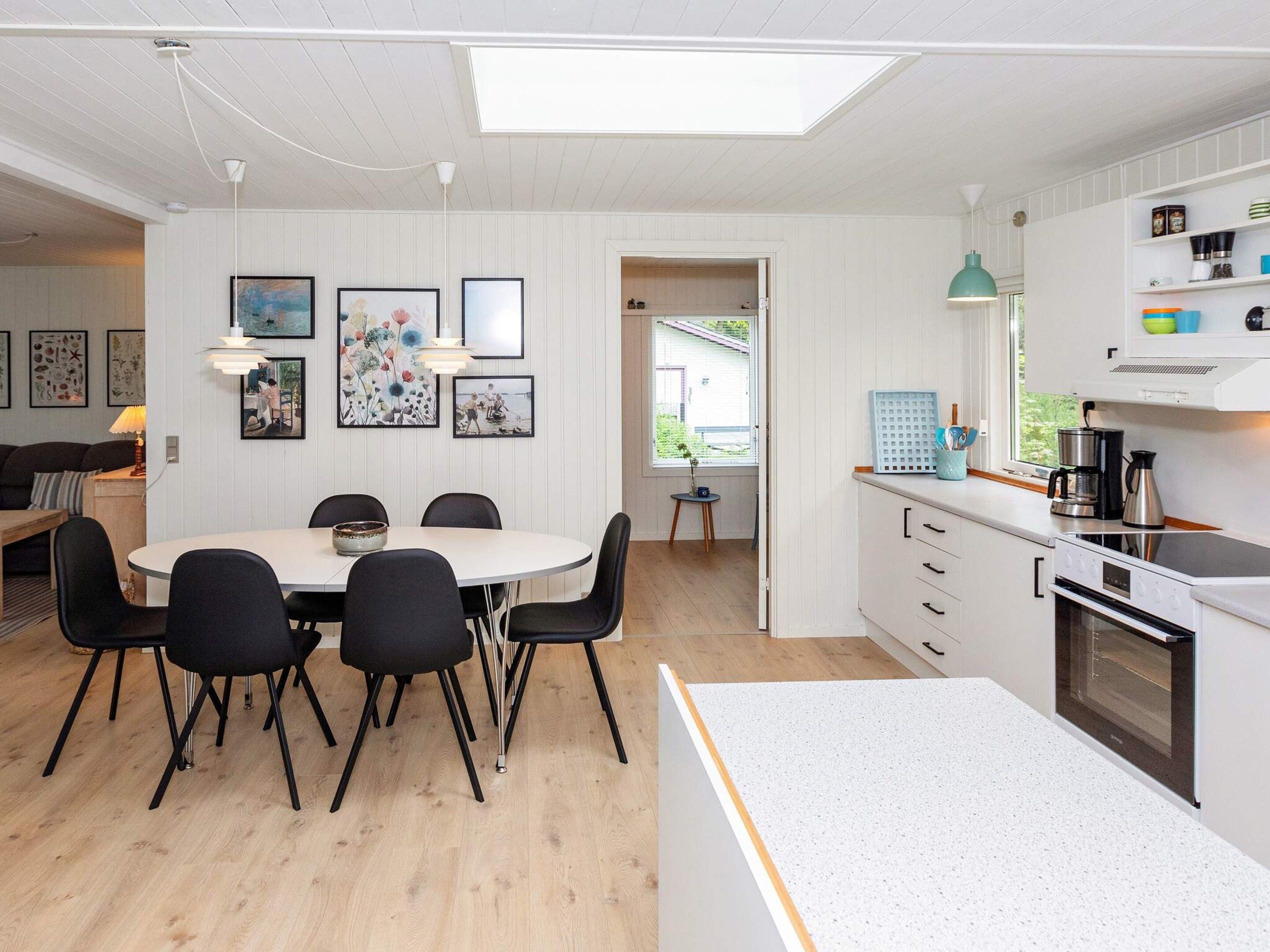 A modern kitchen with a dining area, white cabinetry, and a skylight.