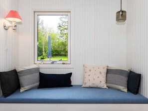 Une pièce avec une fenêtre, un canapé bleu orné de coussins à motifs, une lampe fixée au mur et un luminaire suspendu au plafond.