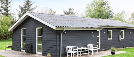 A single-story building with a dark exterior, a sloped roof, and a small porch with outdoor seating.