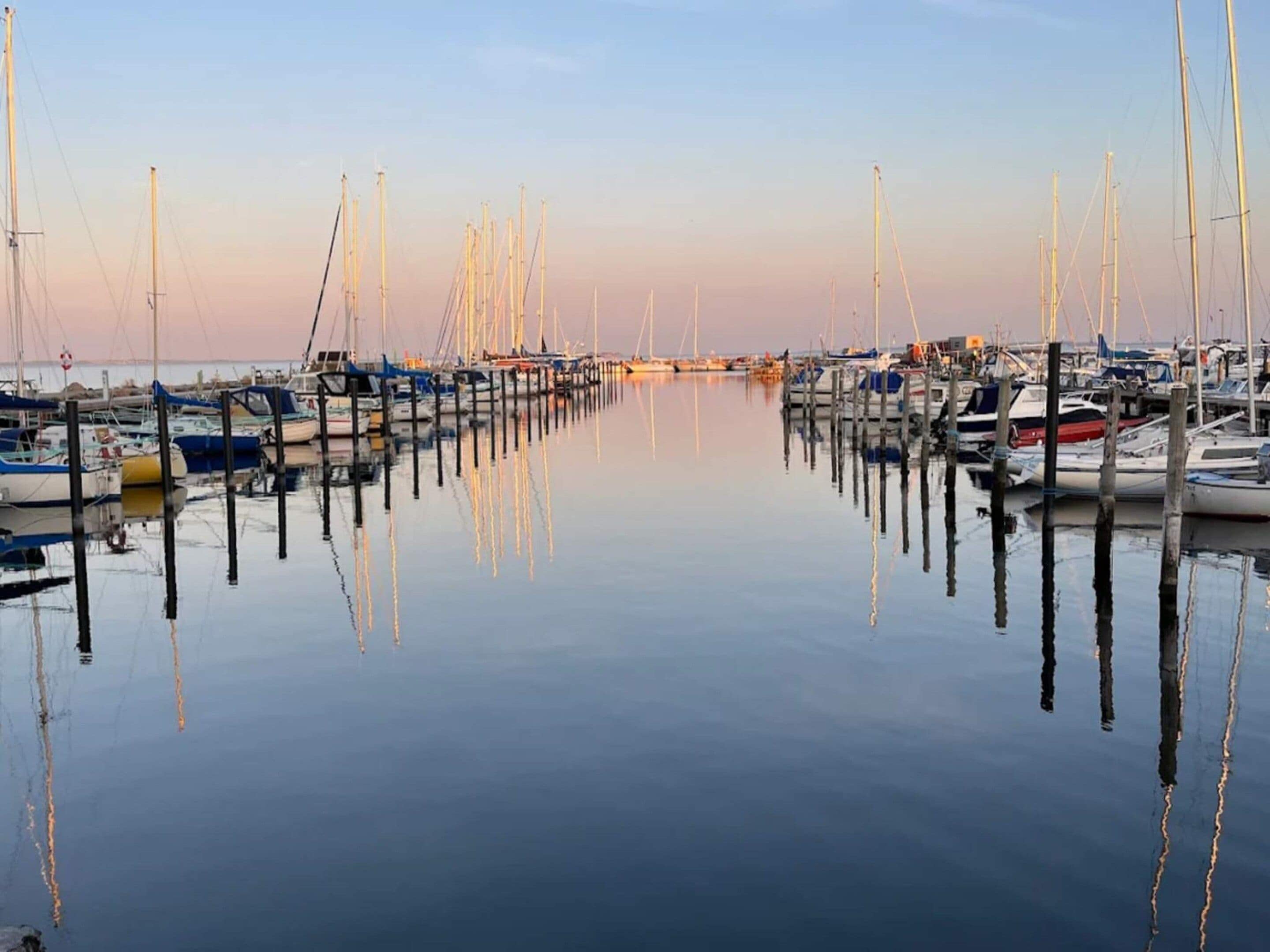 A marina with boats docked at wooden piers, calm water, and a clear sky.