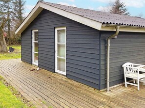 A small, dark wooden cabin with a sloped roof, a wooden deck, and a white bench outside. - 6 Person Holiday Home in Veslos (Vesløs)