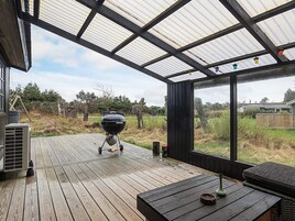 A covered outdoor deck with a grill, a table, and a view of the surrounding landscape.