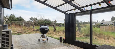 Uma área externa coberta com churrasqueira, mesa e vista para a paisagem ao redor.