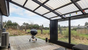 A covered outdoor deck with a grill, a table, and a view of the surrounding landscape.