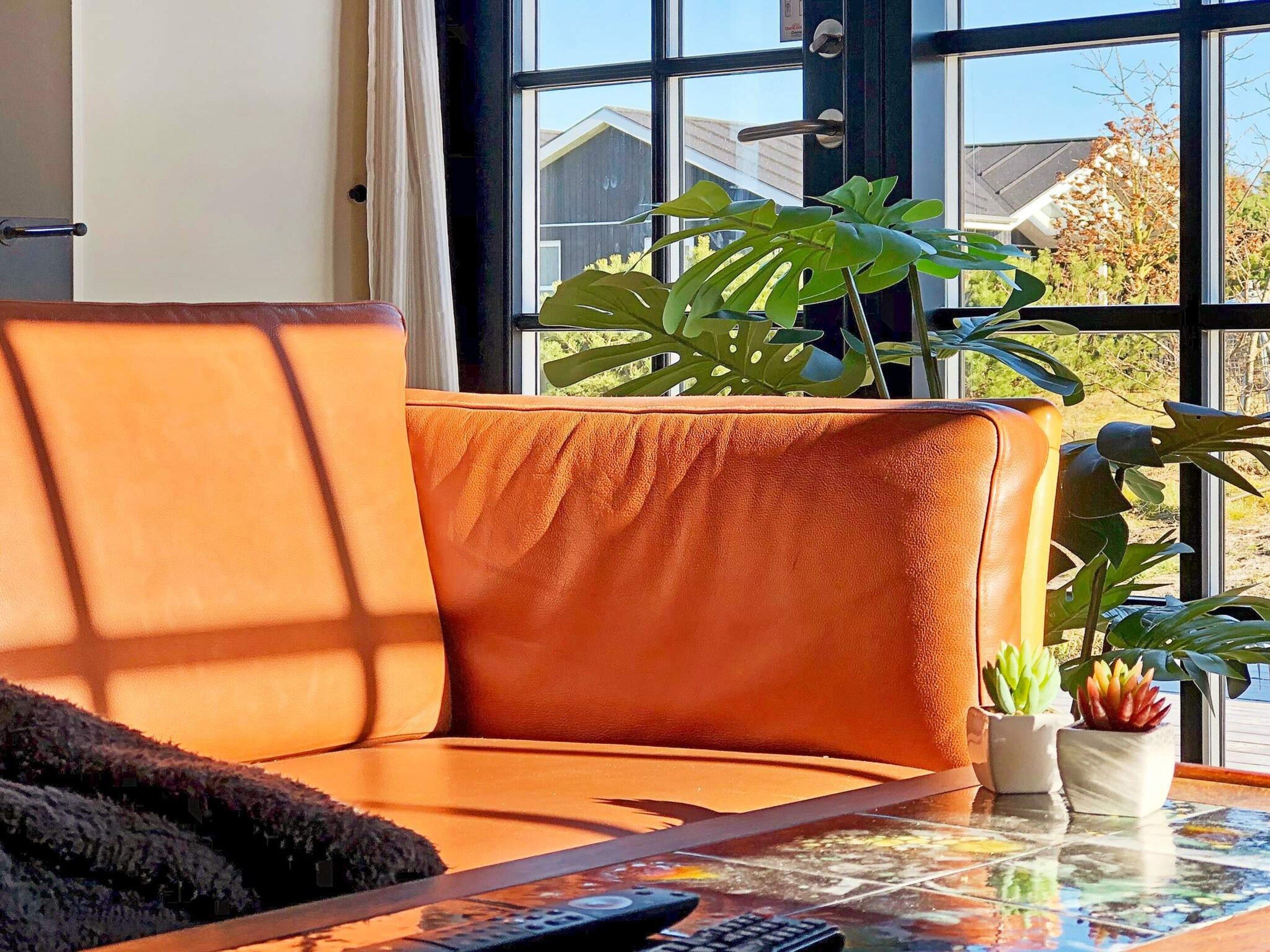 A room with a large window, a sofa, and a table with a remote control.