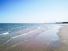 A beach with clear water, a sandy shore, and a distant shoreline.