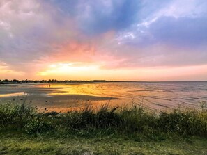 A beach with a sunset, grassy foreground, and distant shoreline. - 4 Star Holiday Home in Hadsund (Hadsund)
