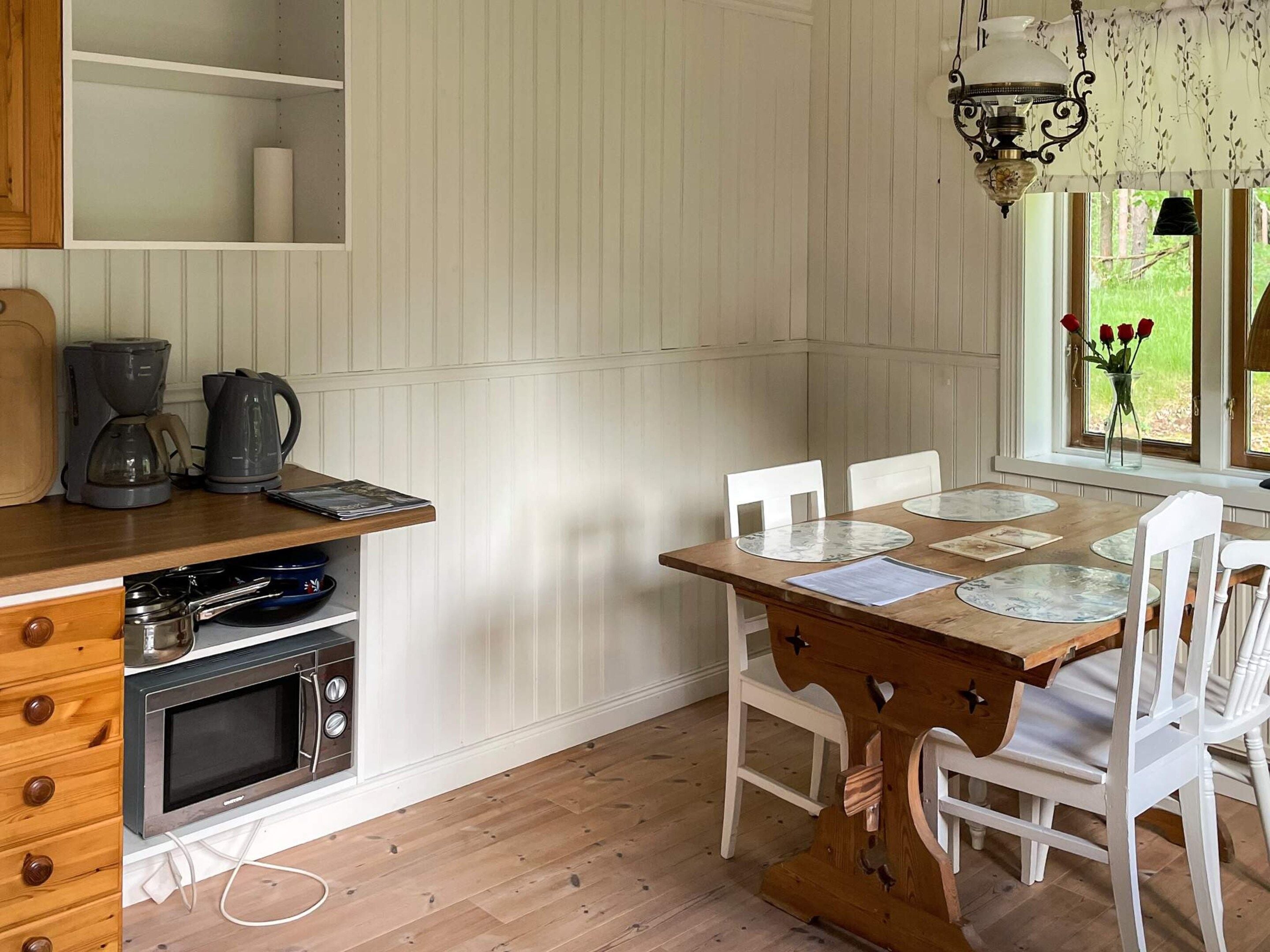 A kitchen with a wooden table, white chairs, a coffee maker, and a hanging light fixture.