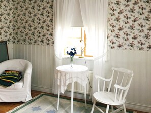 A room with a white chair, a small table with a vase, and floral wallpaper. - 3 Person Holiday Home in Eskilstuna (Eskilstuna)