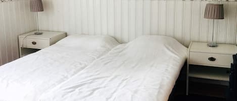 A double bed with a white duvet, two bedside tables with lamps, and a floral wallpaper pattern.