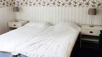 A double bed with a white bedspread, two bedside tables with lamps, and a floral wallpaper pattern.