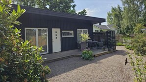 A modern black building with a gravel driveway, a fenced patio area, and surrounding greenery. - 4 Star Holiday Home in Farhult (Hoganas)
