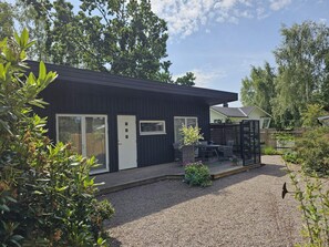 A modern black building with a gravel driveway, a fenced patio area, and surrounding greenery. - 4 Star Holiday Home in Farhult (Hoganas)
