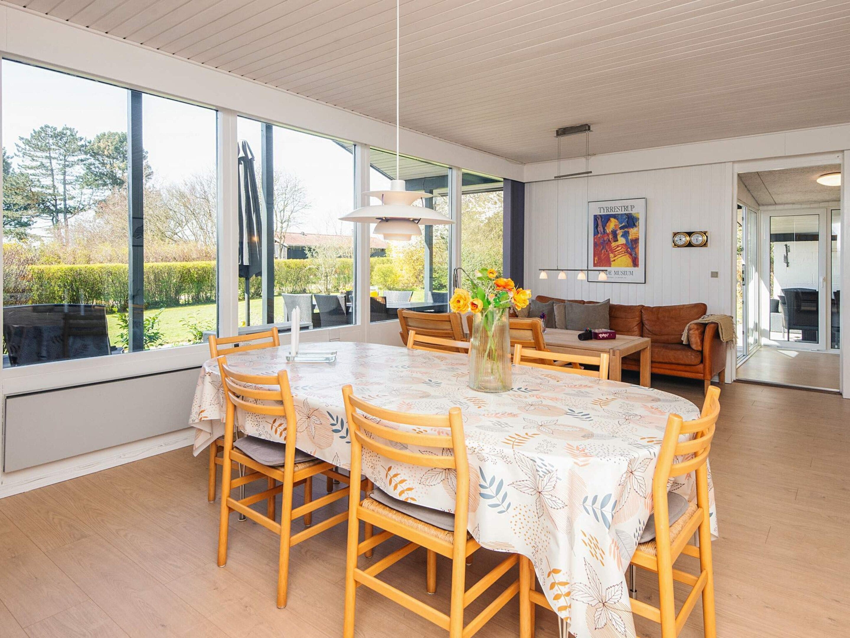 A dining area with a table and chairs, a vase with flowers, and a sofa.