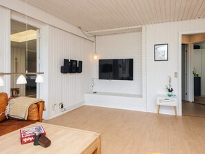 A modern living room with a TV, wooden flooring, a sofa, a coffee table, and a small side table with a plant.