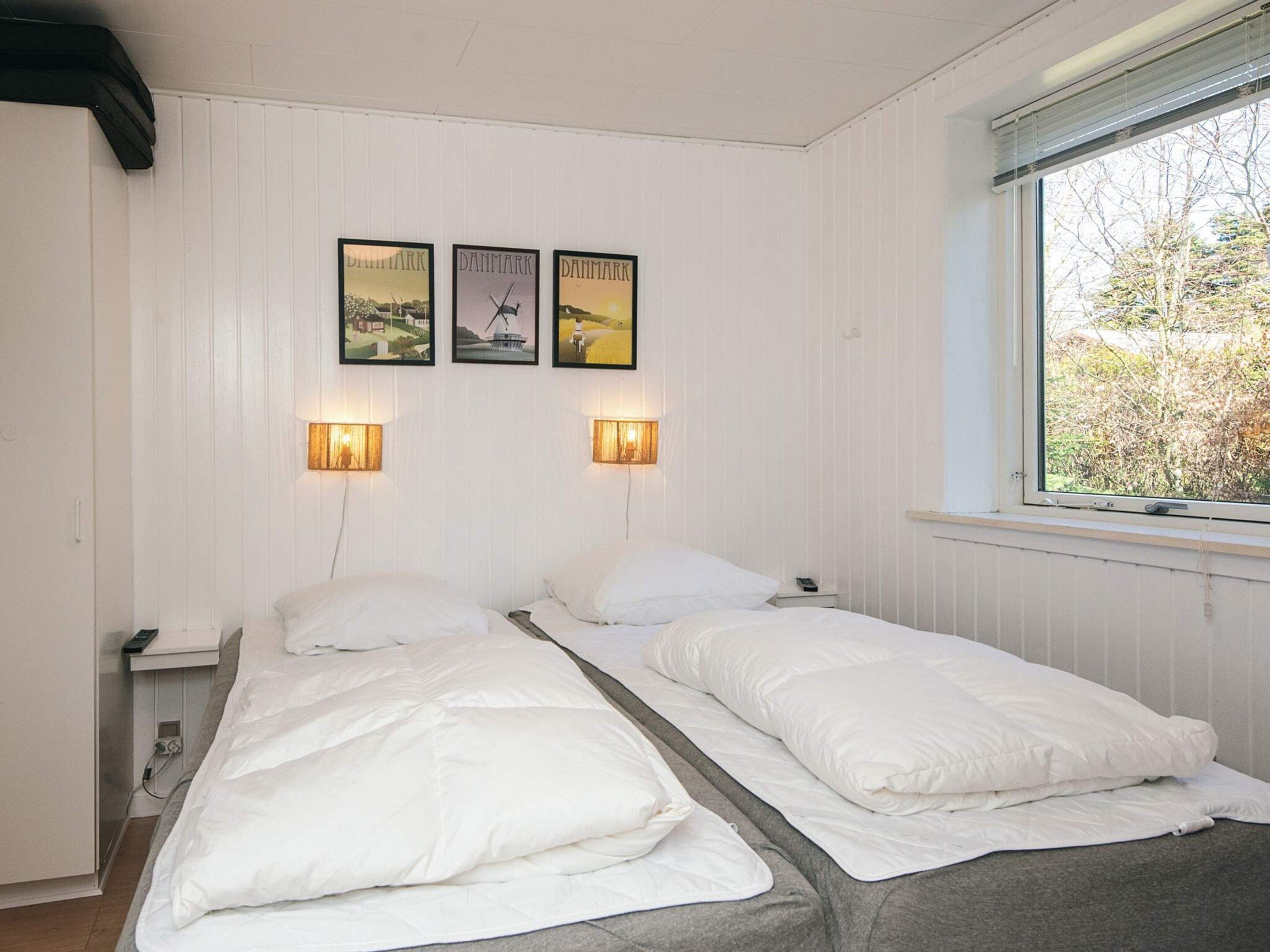 A room with two beds, a window with a view of trees, and three framed pictures on the wall.