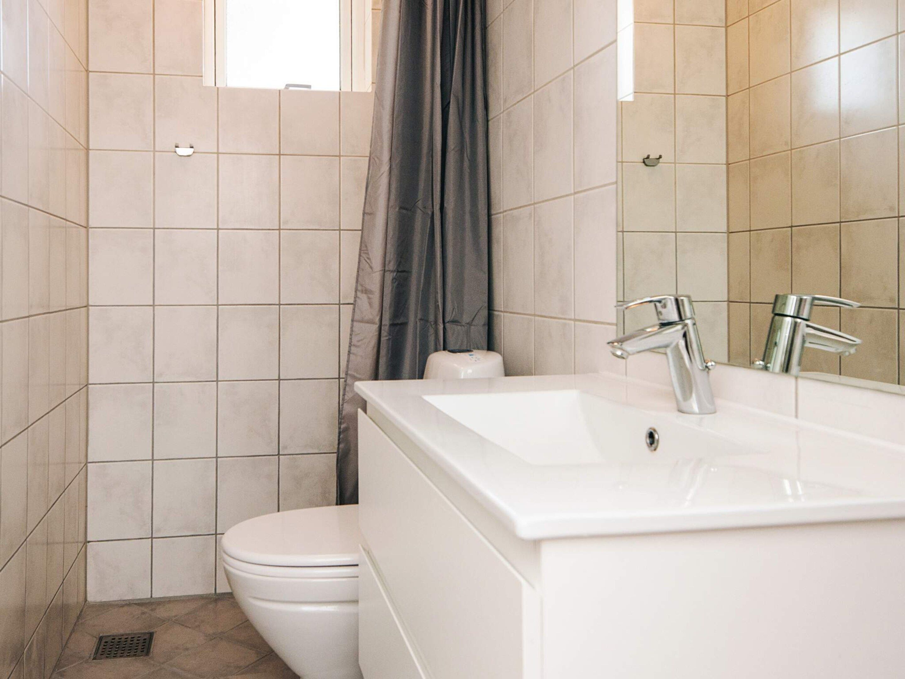 Et badeværelse med en hvid vask, to vandhaner, et toilet og en badeforhæng.