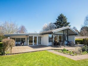 Ett modernt hus med en täckt uteplats, en gräsmatta och en trädgård.