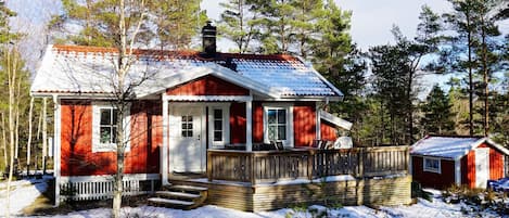 A red wooden cabin with a porch, surrounded by trees and snow.