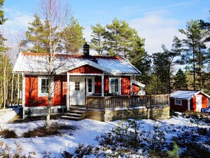 Une cabane en bois rouge, dotée d’un porche, entourée d  ’arbres et de neige.