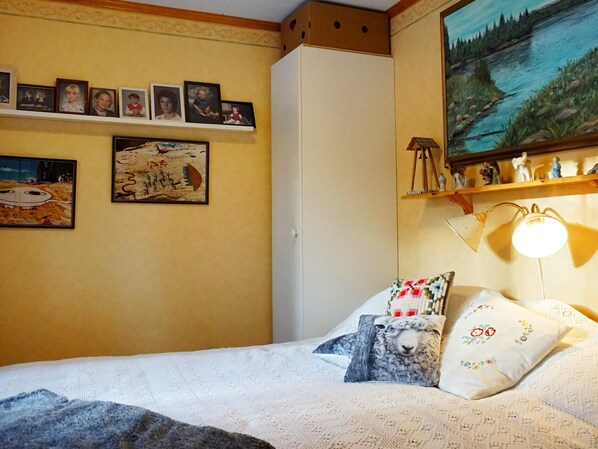 Une chambre à coucher avec un lit, des oreillers, une lampe, une étagère avec des figurines et des tableaux encadrés accrochés au mur.