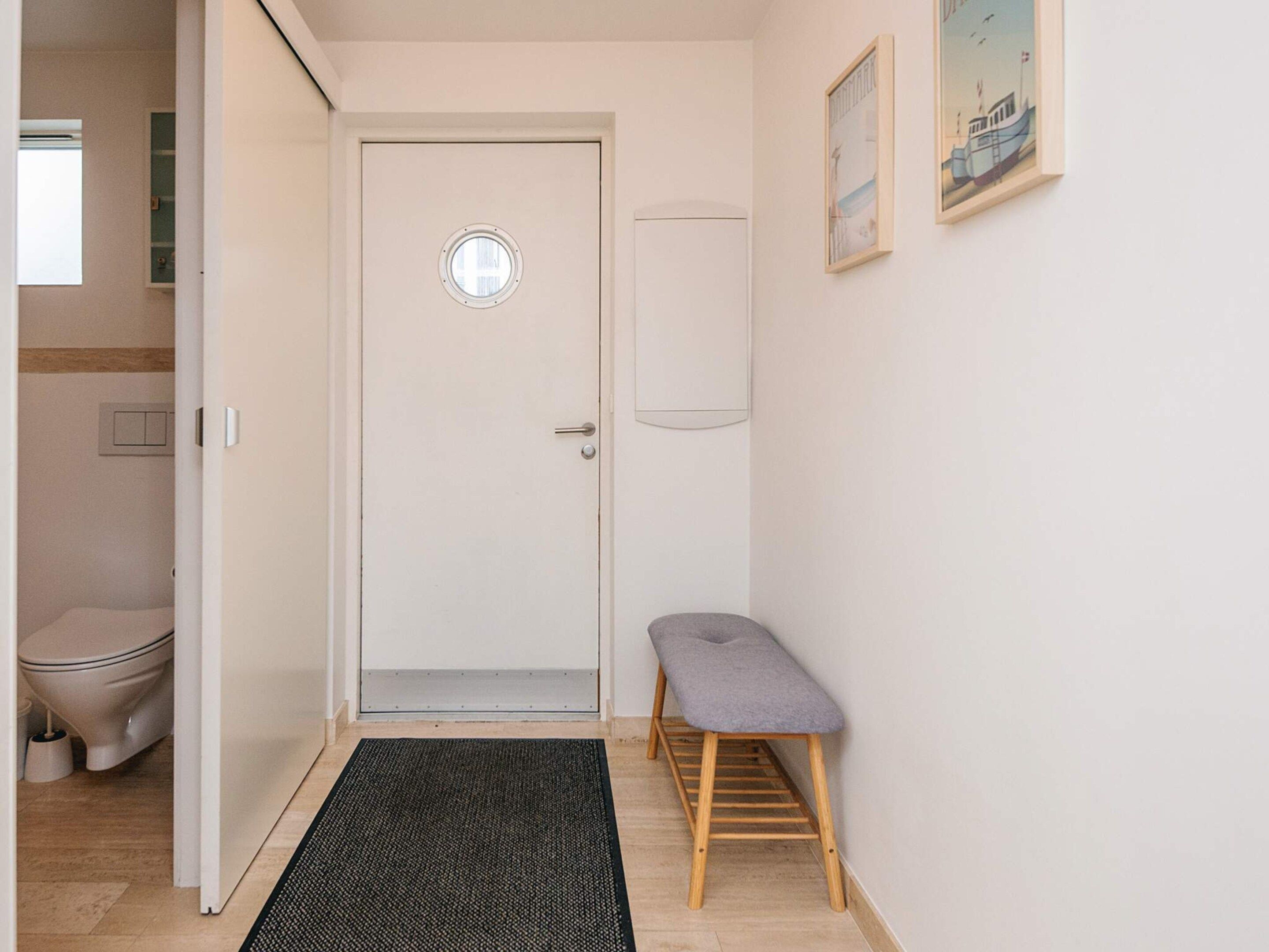 A narrow hallway with a door, a small bench, a doormat, and a wall-mounted picture.