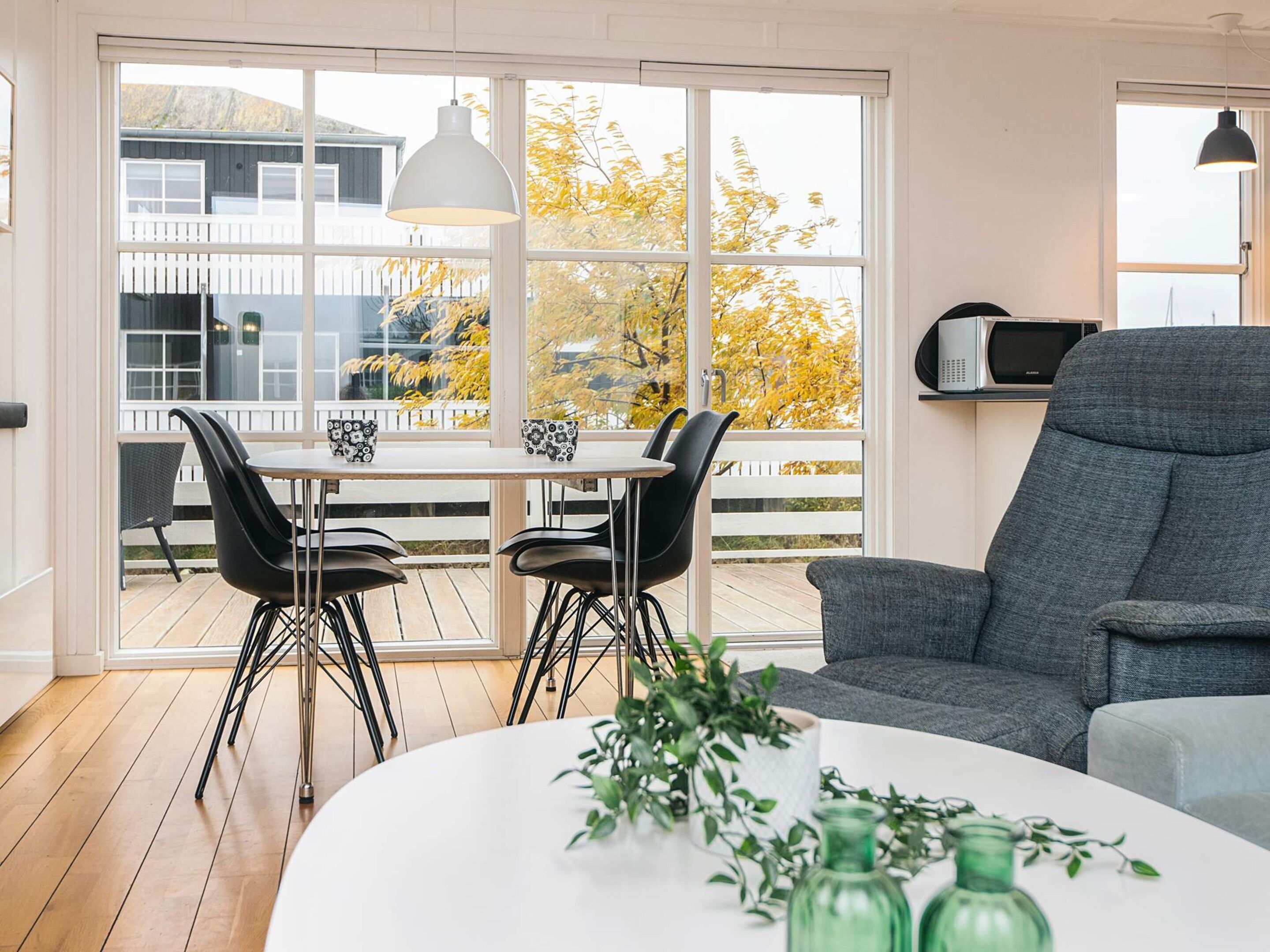 A modern living room with a dining area, large windows, and a view of a house and trees.
