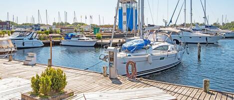 A marina with multiple boats docked, a wooden deck with a table and benches, and a small building with a blue roof.
