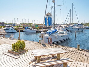 A marina with multiple boats docked, a wooden deck with a table and benches, and a small building with a blue roof. - 4 Star Holiday Home in Ebeltoft (Ebeltoft)