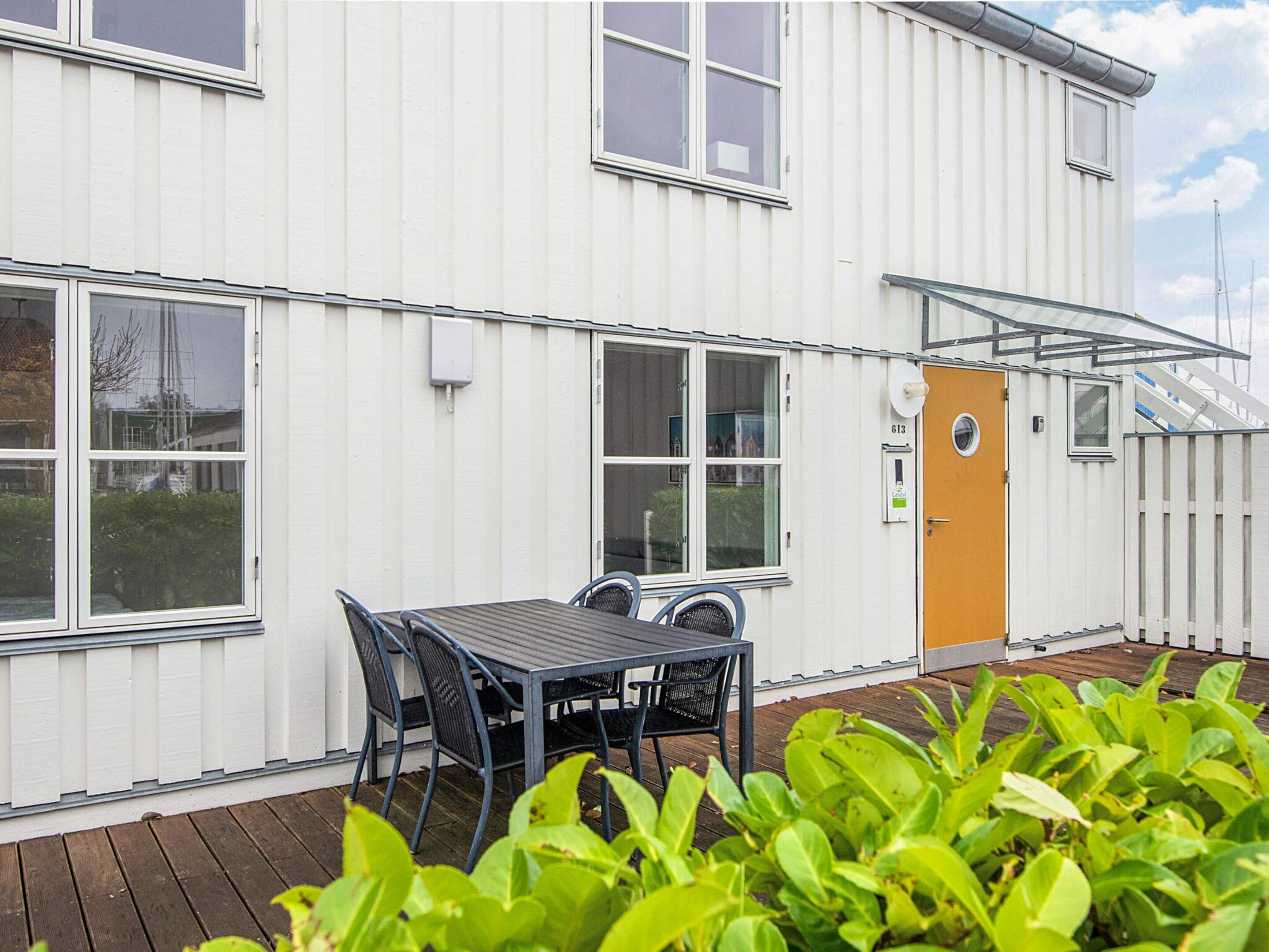 A white building with a wooden deck, a table with chairs, and a door with a window.