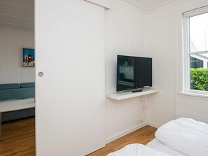 A room with a television on a white shelf, a blue sofa, and a window with a view of greenery. - 4 Star Holiday Home in Ebeltoft (Ebeltoft)