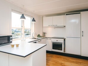 A modern kitchen with white cabinets, a black countertop, a built-in oven, a microwave, and pendant lights.