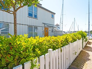 A white building with a wooden door, surrounded by a white picket fence and lush green bushes. - 4 Star Holiday Home in Ebeltoft (Ebeltoft)