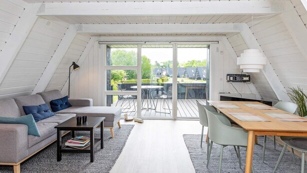 Habitación tipo ático con sofá, mesa de centro, mesa de comedor y sillas. Hay un amplio ventanal corredero que da a un patio exterior con mesa y sillas.