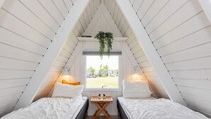 Un dormitorio acogedor en el ático, con dos camas, una ventana y una planta colgante.